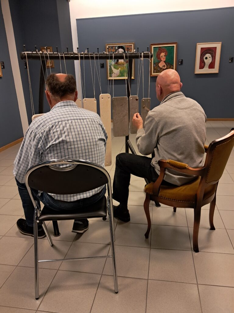 Odprtje razstave Odtisi v kamnu. Dva moška sedita in igrata na pojoče kamne.