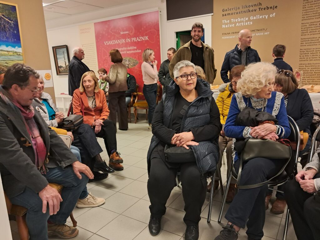 Odprtje razstave Odtisi v kamnu. Ljudje sedijo in se pogovarjajo.