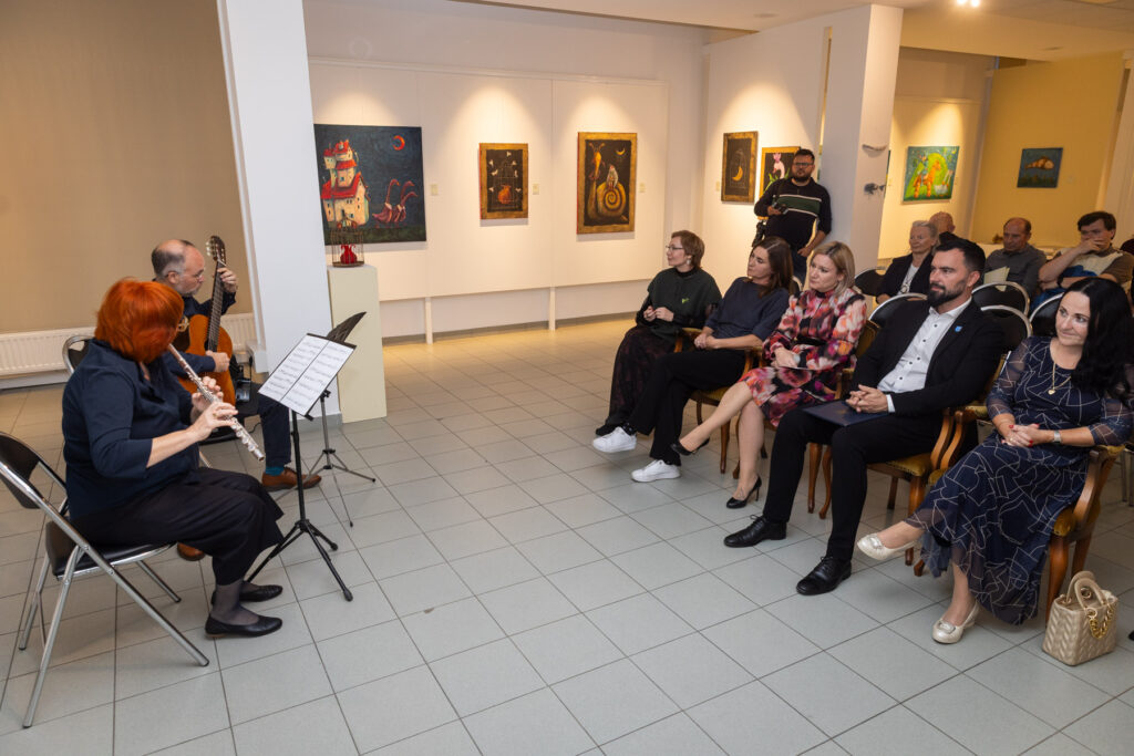 Glasbenika, ki se imenujeta Duo Limonium na otvoritvi razstave Natalie Berezina igrata flavto in kitaro. Obiskovalci ju sede poslušajo.